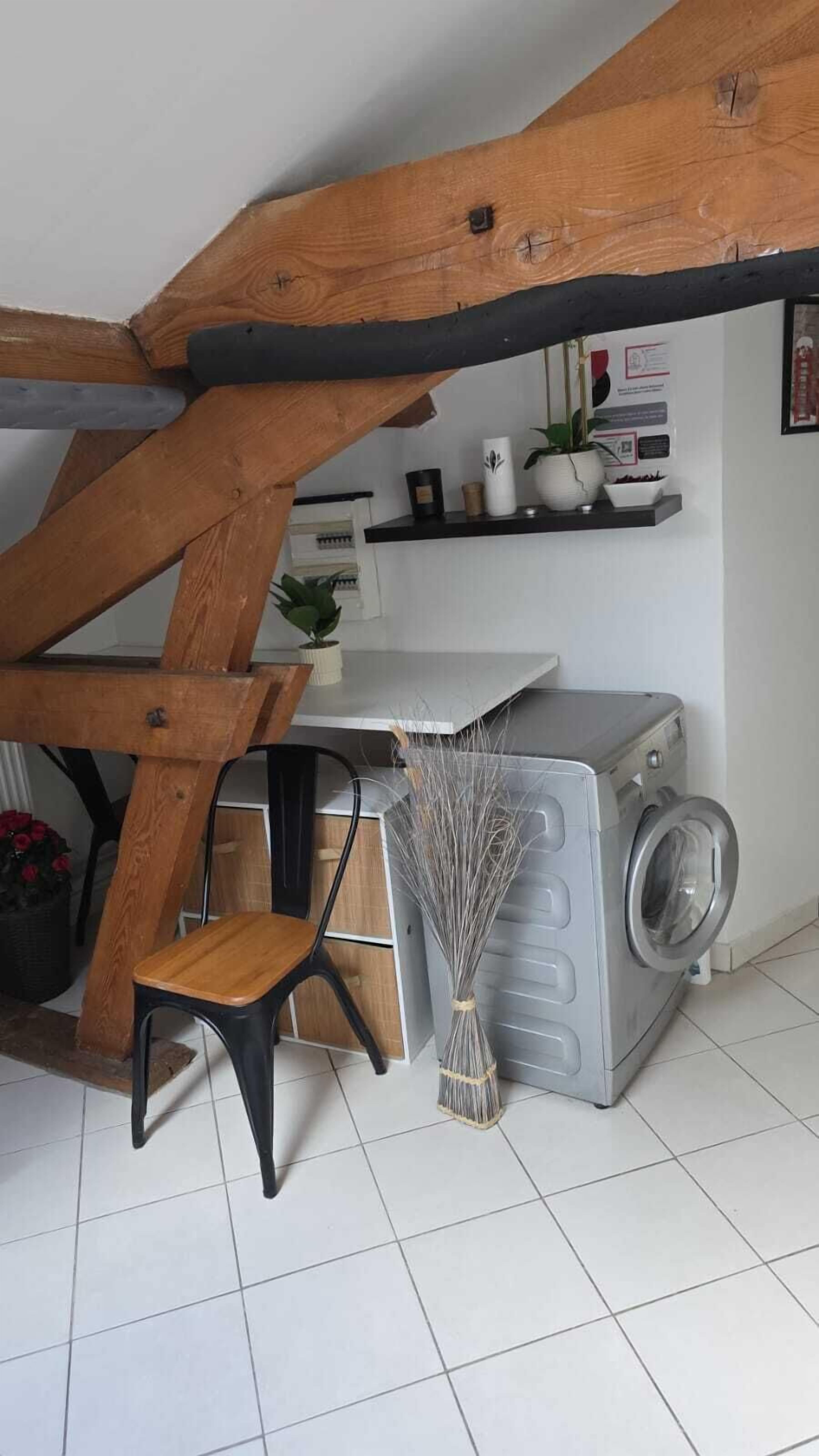 Un área de lavandería con lavadora, escoba, silla y estante con objetos.