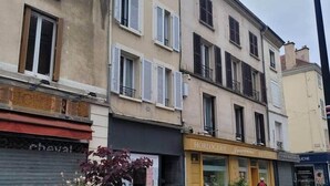 A street view with a building featuring a storefront with a sign that reads "HORLOGERIE."