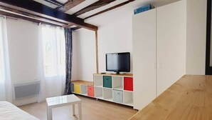 A room with a bed, a small white table, a TV on a wooden shelf, and a wardrobe.