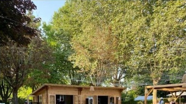 A small wooden structure with outdoor seating, surrounded by trees and a grassy area.