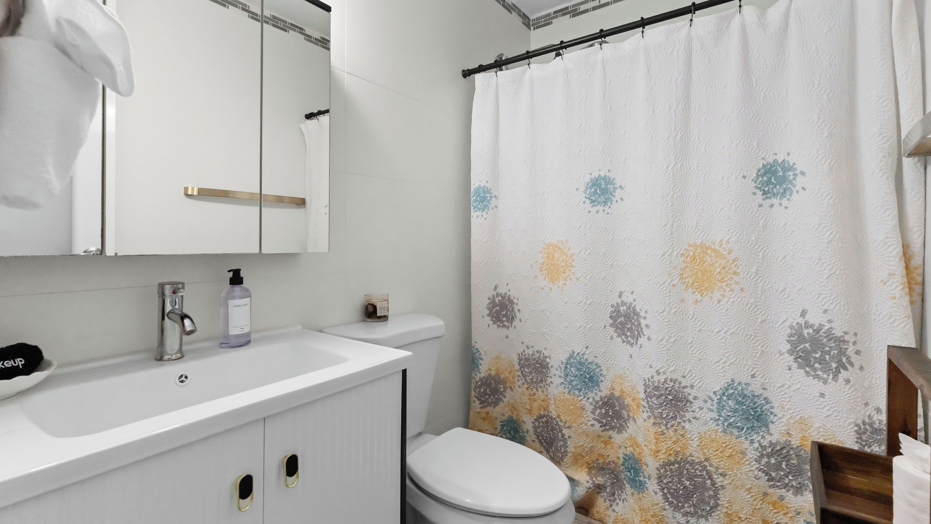 Un baño con lavamanos blanco, inodoro y cortina de ducha con estampado floral.