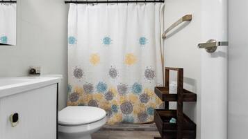 A bathroom with a shower curtain featuring a floral pattern, a white toilet, a wooden shelf with a mirror, and a white sink.