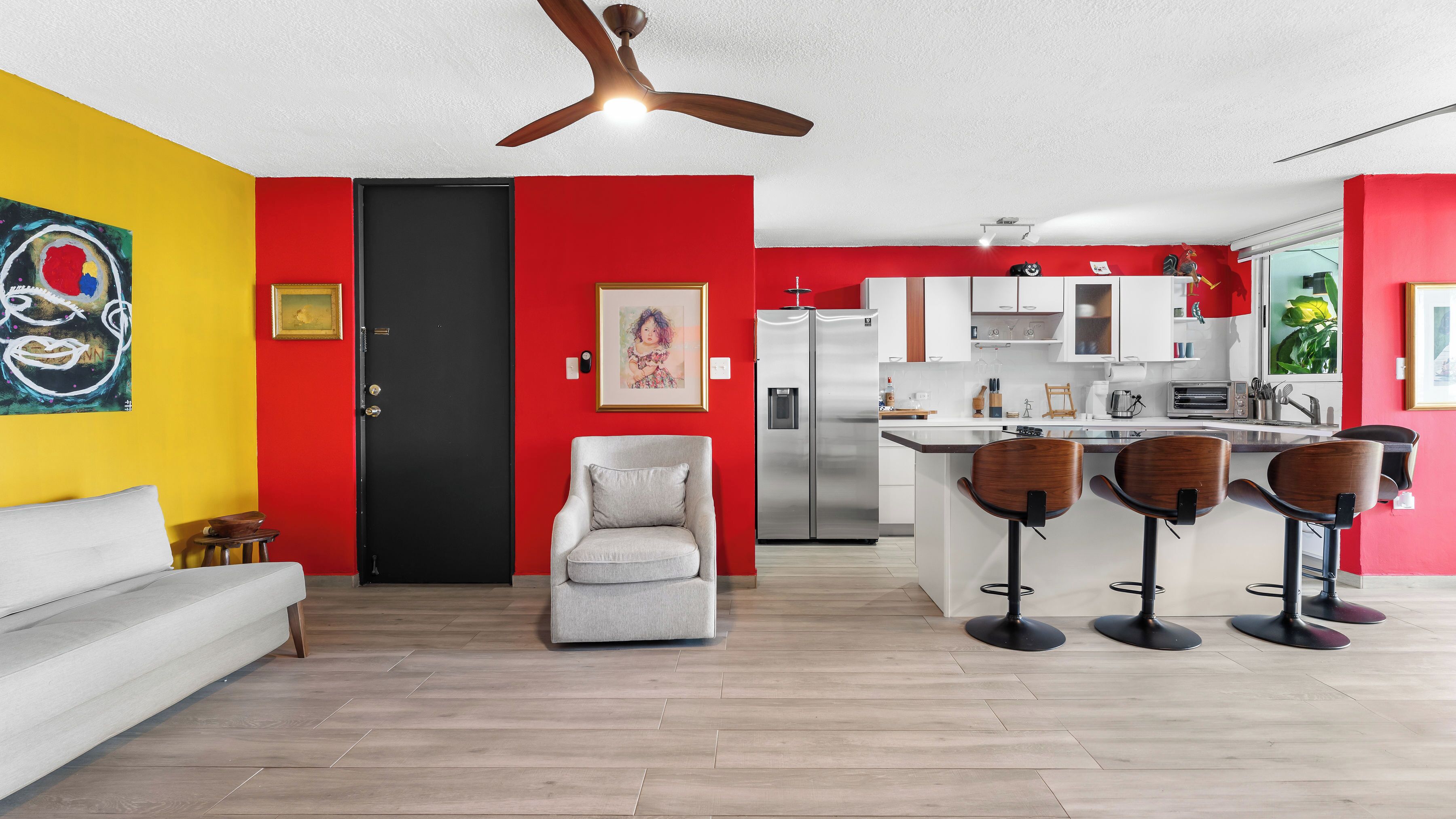 A modern kitchen with a refrigerator, microwave, and sink. There is a dining area with bar stools and a sofa.