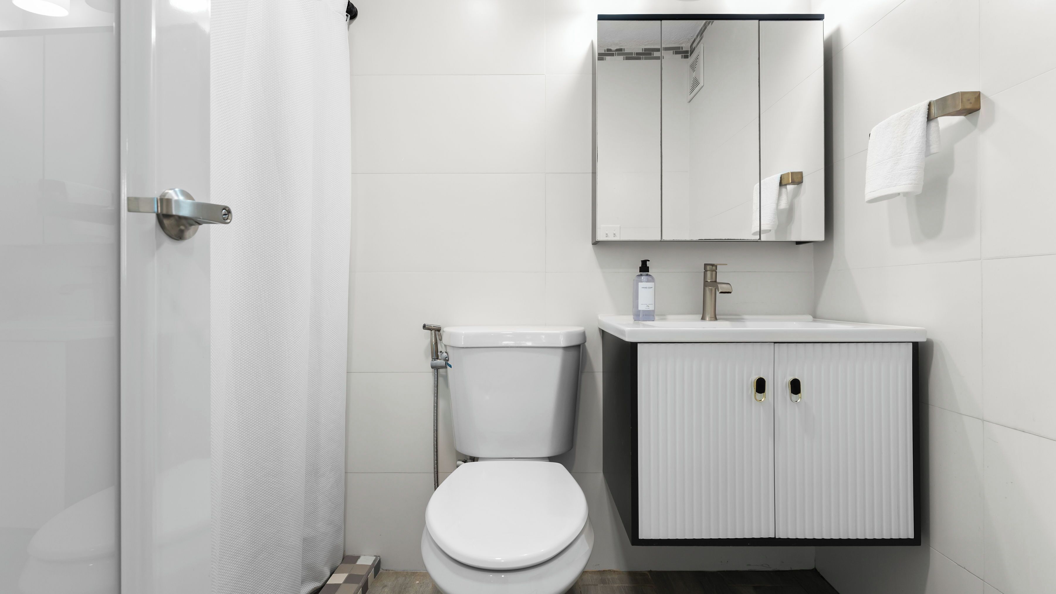 A modern bathroom with a white toilet, a shower, a sink with a mirror above, and a towel rack.
