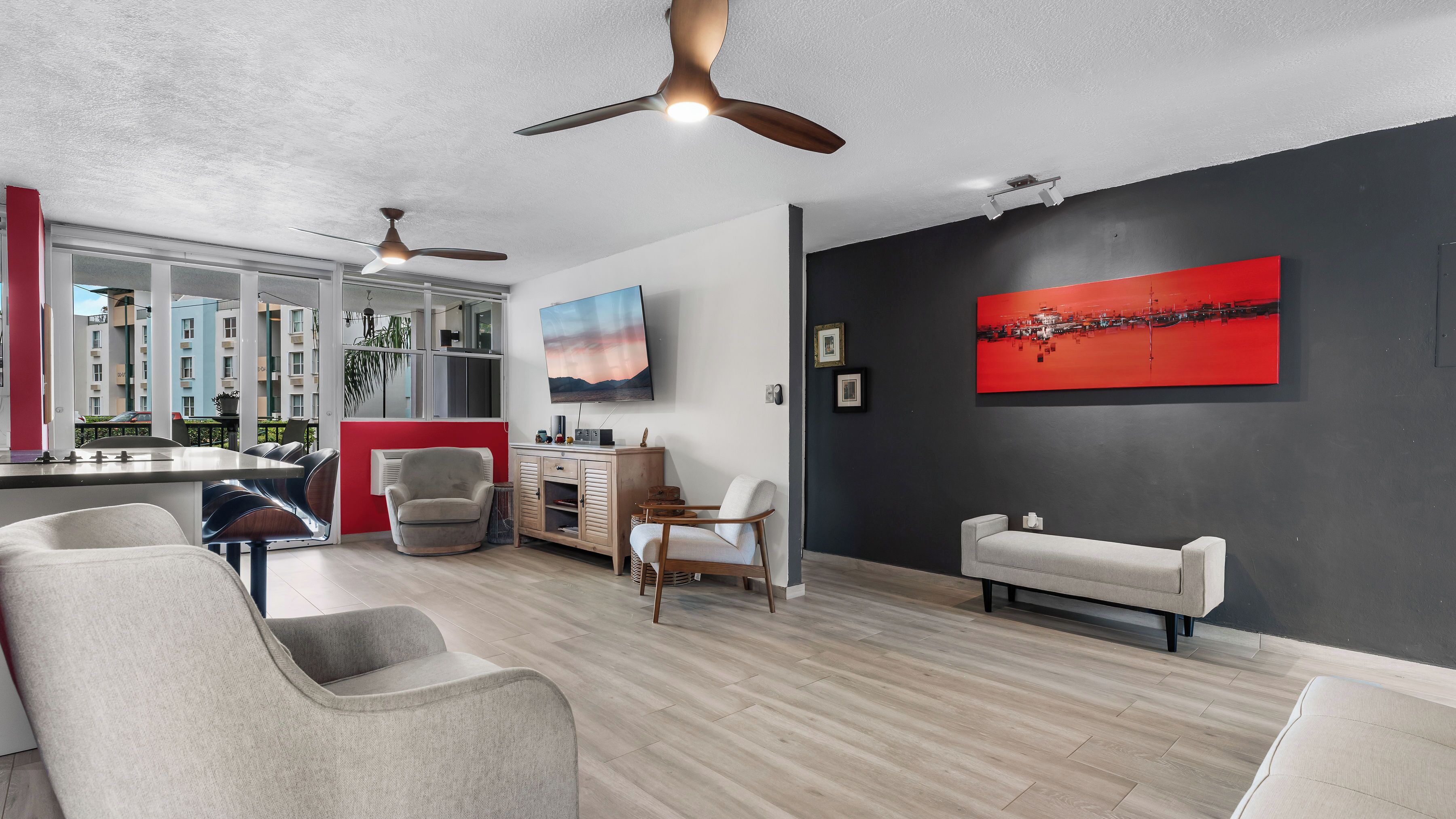 Una sala de estar moderna con un televisor grande, una obra de arte roja y un ventilador de techo.