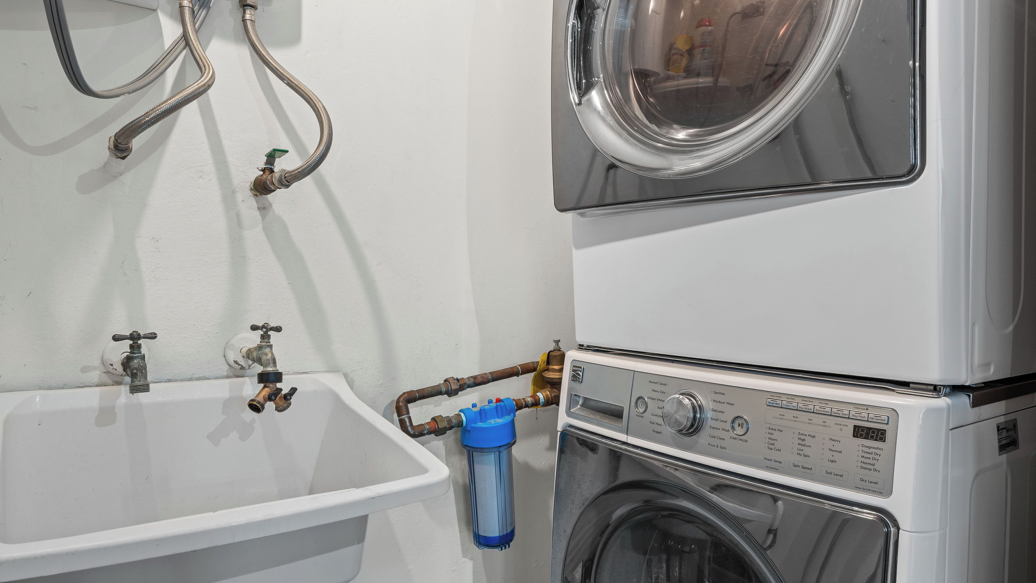 Un espace dédié à la lessive, équipé d’une machine à laver, d’un évier et de tuyaux d’eau.