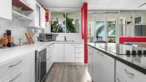Une cuisine moderne avec des armoires blanches, un four encastré et un mur d’accent rouge.