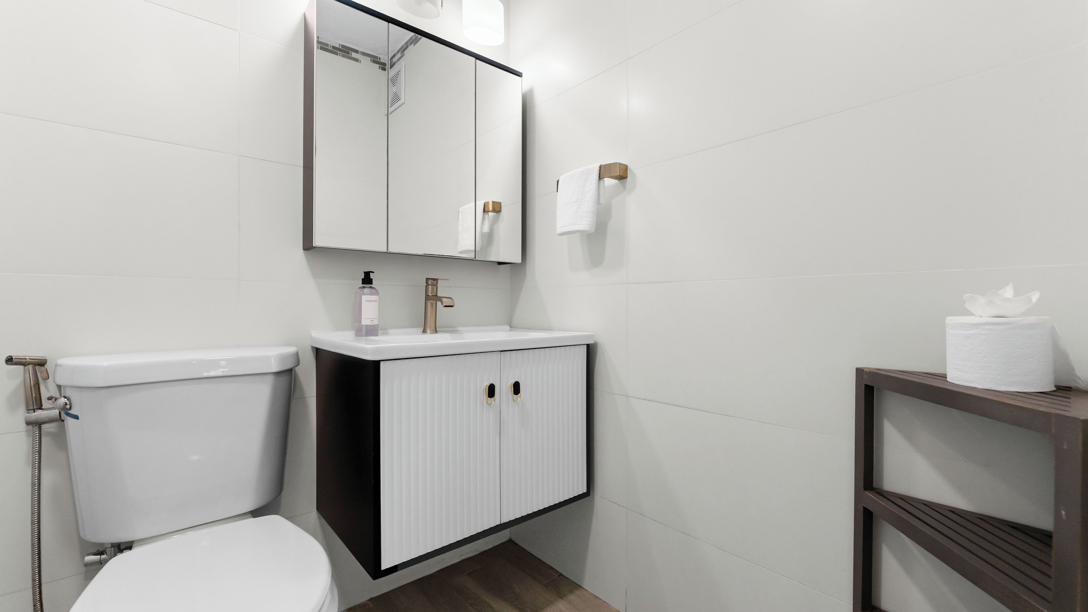 Une salle de bain moderne avec des toilettes blanches, un lavabo surmonté d’un miroir et un porte-serviettes.