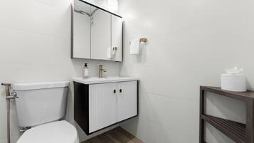 Une salle de bain moderne avec des toilettes blanches, un lavabo surmonté d’un miroir et un porte-serviettes.