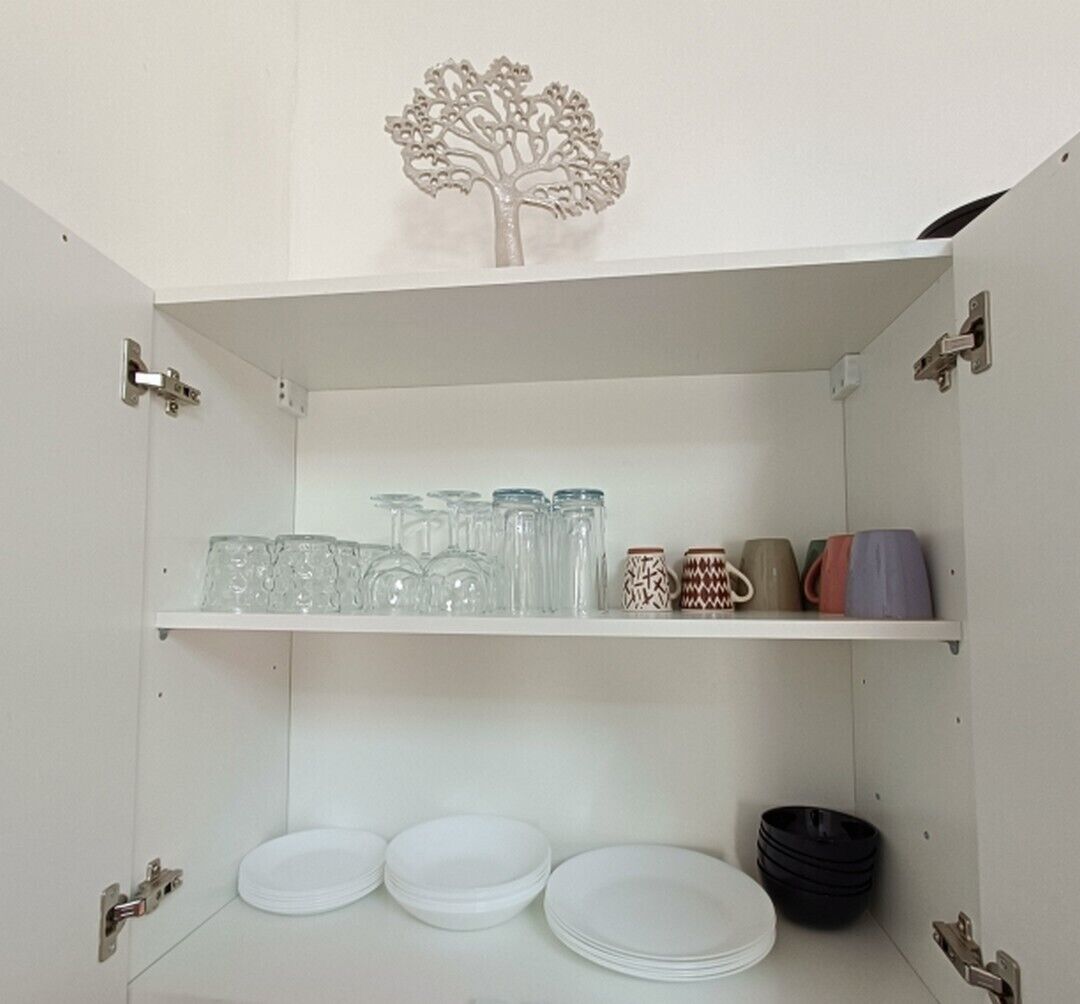 A white cabinet with shelves holding glassware, plates, and mugs.