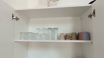A white cabinet with shelves holding glassware, plates, and mugs.