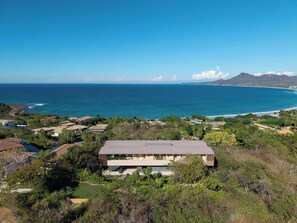 A modern house with a flat roof, surrounded by lush greenery and overlooking a coastal area with mountains in the distance. - Casa Tukipa: 4BR High-End Villa w/ Private Pool (Punta Mita)