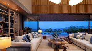 Uma sala de estar moderna com uma janela grande voltada para uma praia e montanhas.