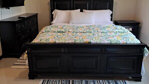 A bedroom with a dark wooden bed, a television on the wall, a nightstand, and a dresser. - 2-bedroom condo in delightful Kingston with cool AC (Kingston)
