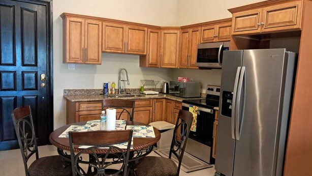 A kitchen with wooden cabinets, a stainless steel refrigerator, a microwave, and a stove. There is a dining table with chairs and a roll of paper towels on it. - 2-bedroom condo in delightful Kingston with cool AC (Kingston)