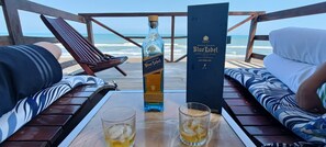 Un área de estar frente a la playa, con una mesa que presenta una botella de Johnnie Walker Blue Label y dos vasos de whisky.