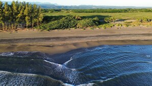 Paisaje costero con una playa, olas y montañas a lo lejos.