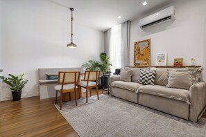 A living room with a sofa, two chairs, a dining table, a hanging light fixture, a potted plant, and an air conditioning unit. - Sanci Mare: 1 bedroom and 2 bathrooms in Copacabana   (Rio de Janeiro)