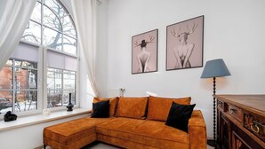 Ein modernes Wohnzimmer mit großem Fenster, einem Ecksofa, einer Holzkommode und zwei gerahmten Bildern an der Wand.