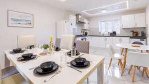 Une cuisine moderne avec des meubles blancs, un coin repas avec une table blanche dressée pour quatre personnes, et une petite table à manger avec deux chaises.