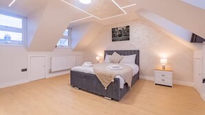 Une chambre moderne avec un plafond en pente, un grand lit, des tables de chevet avec des lampes et une vue sur la ville à travers une lucarne.