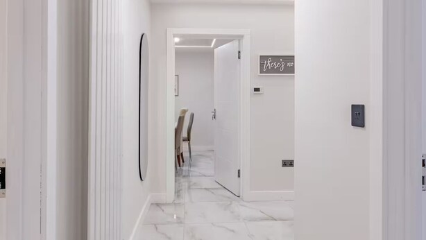 Un couloir aux murs blancs, doté d’un sol en marbre et d’un éclairage encastré.
