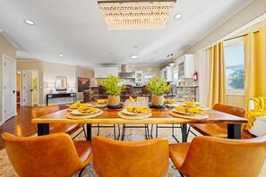 Un comedor con una mesa de madera dispuesta para seis personas, rodeado de sillas color naranja, y dos plantas en macetas sobre la mesa.