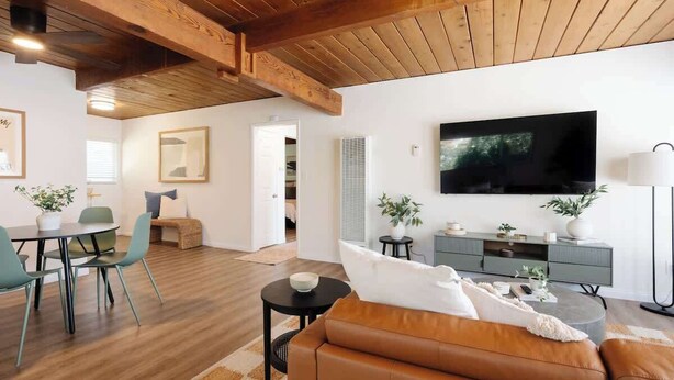 Ein modernes Wohnzimmer mit Holzboden, einem Flachbildfernseher, einer Couch, einer Essecke mit Stühlen und einem kleinen Tisch.