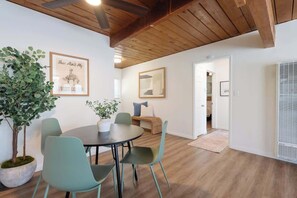 A dining area with a round table, four chairs, and a potted plant. There are framed pictures on the wall and a ceiling fan above. - Central Charm & Style | Walk to Lil Italy & Trails (San Diego)