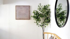 Una habitación con un banco de madera, una obra de arte enmarcada, una planta en maceta, un espejo y una lámpara en el techo.
