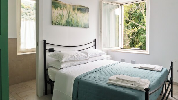 Une chambre à coucher avec un lit, du linge de lit blanc, une couvre-lit turquoise et un tableau représentant de l’herbe sur le mur.
