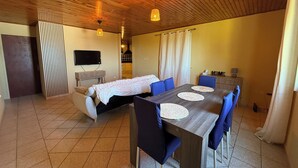 A modern room with a wooden ceiling, a bed with a white blanket, a TV mounted on the wall, and a dining area with a table and chairs. - Large 100 m² T3 with garden & sea view - Absolute peace and quiet in Petite-Île (Petite-Île)
