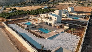 En moderne villa med swimmingpool, udendørs møbler og udsigt over det omkringliggende landskab.