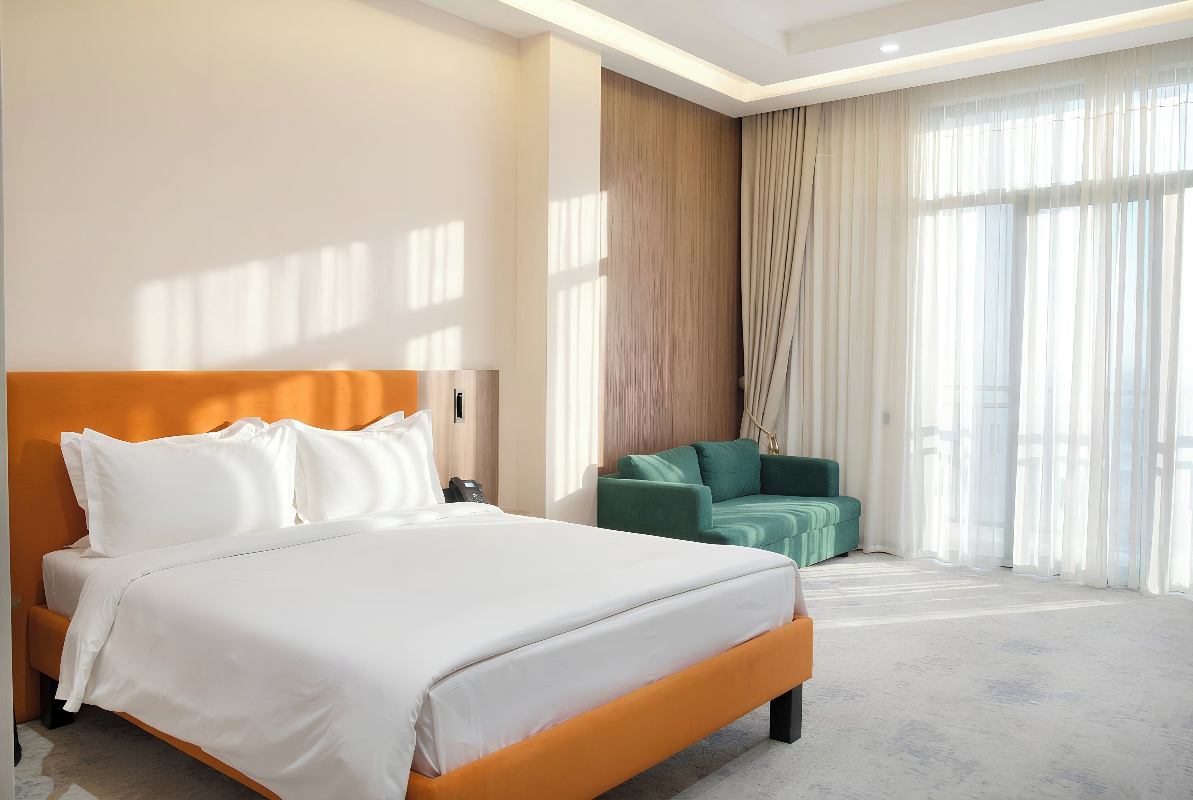 Habitación de hotel con una cama grande, un sofá verde y un ventanal con cortinas.