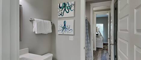 Un baño con inodoro, lavabo y toallero. Hay tres obras de arte en la pared con diseños de pulpo.