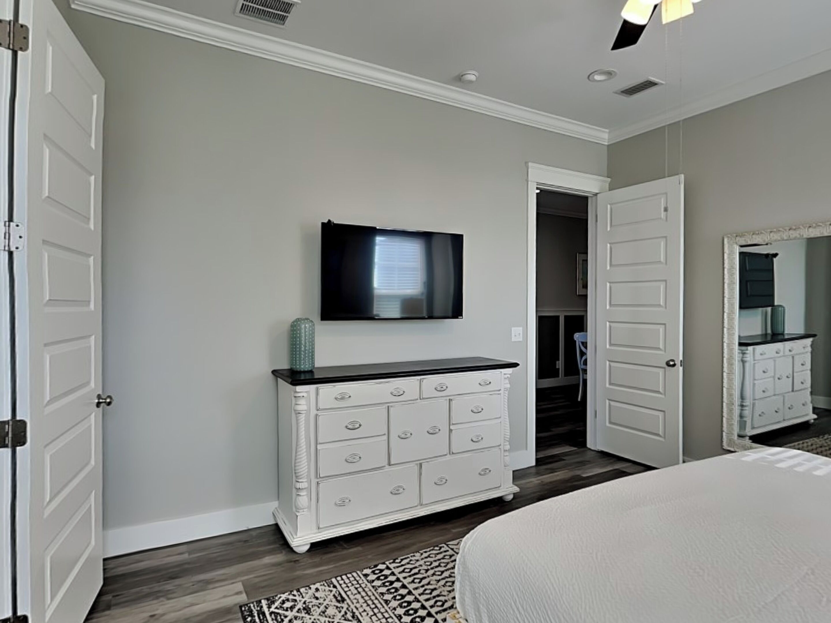 Een slaapkamer met een bed, een dressoir, een televisie en een deur naar een andere kamer.