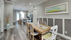 A spacious dining area with a wooden table and striped chairs, a kitchen in the background, and a painting on the wall. - Gone Shellin' (Panama City Beach)