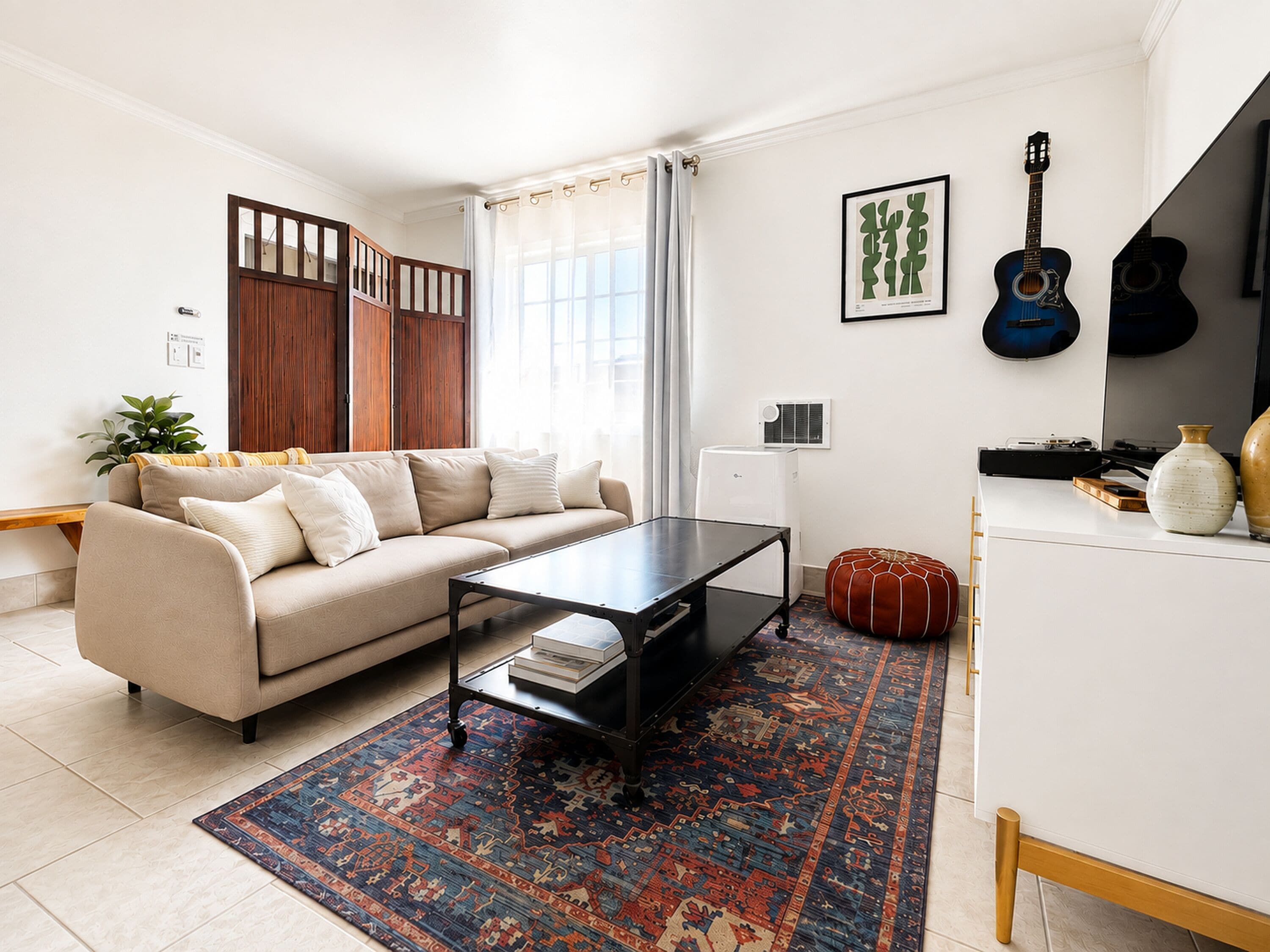 A living room with a sofa, coffee table, rug, and a guitar on the wall.