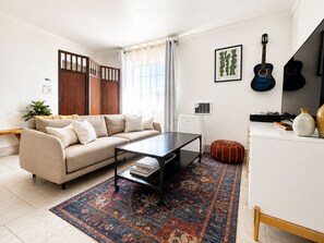 A living room with a sofa, coffee table, rug, and a guitar on the wall. - Downtown Studio FREE Parking & 1 mile to Beach & Convention Center (Long Beach)