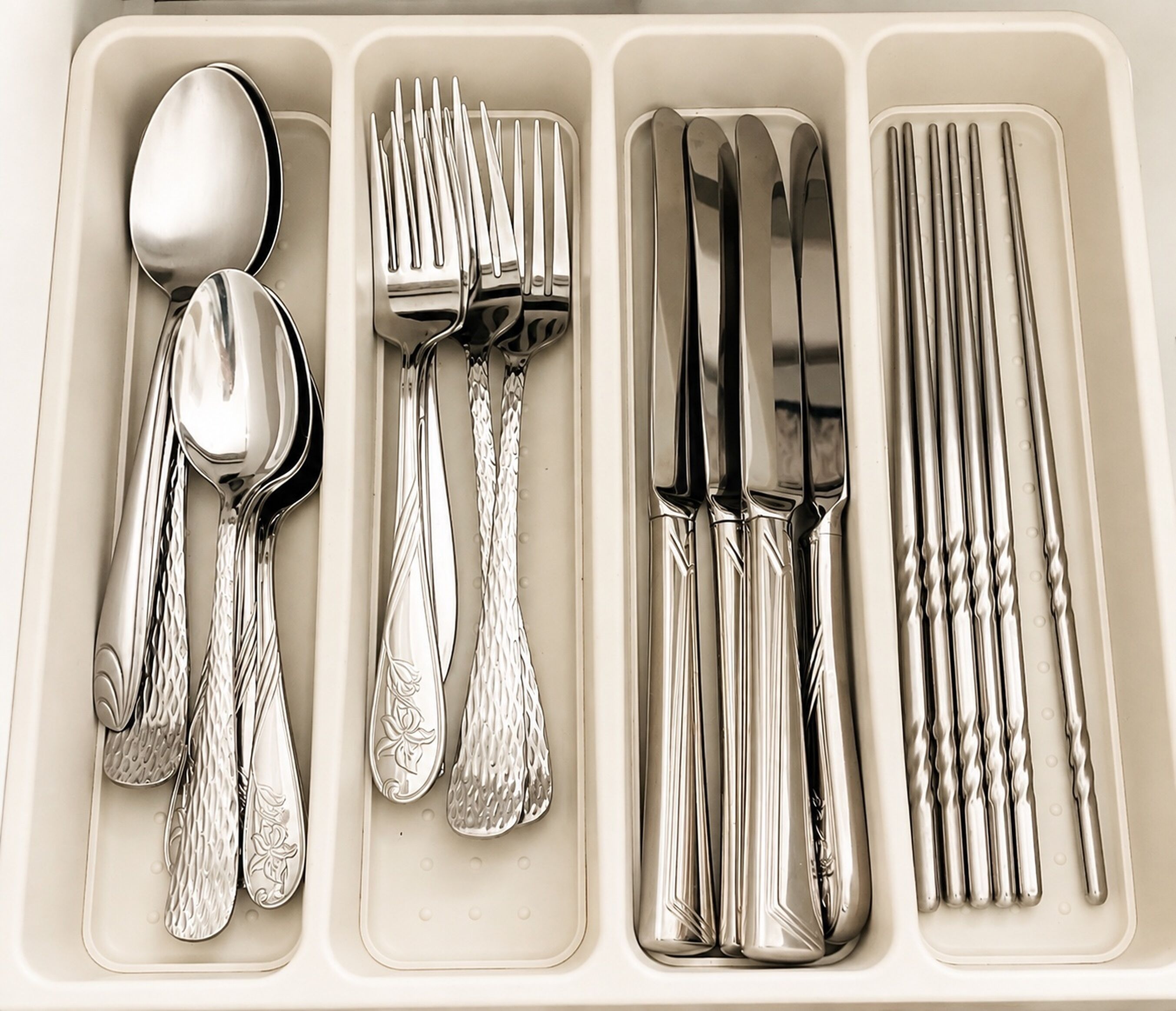 A set of silverware neatly arranged in a compartmentalized tray with spoons, forks, knives, and a set of chopsticks.