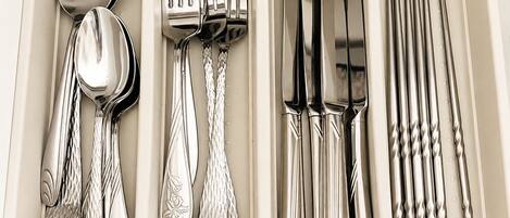 A set of silverware neatly arranged in a compartmentalized tray with spoons, forks, knives, and a set of chopsticks.