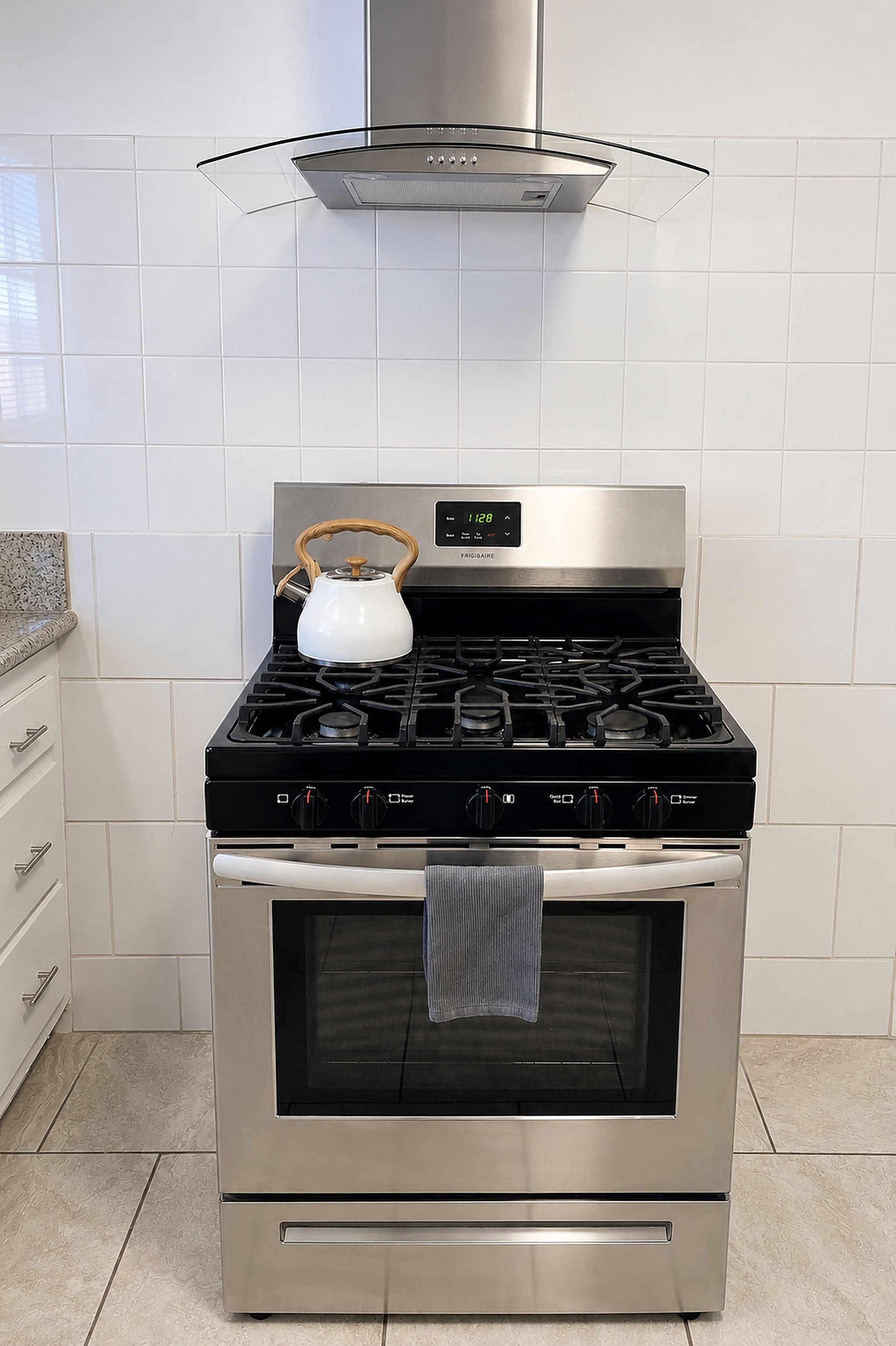 A stainless steel kitchen with a gas stove, oven, and a kettle on the stove.
