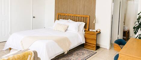 A bedroom with a bed, bedside table, lamp, and a view of a bathroom.