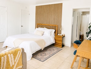 A bedroom with a bed, bedside table, lamp, and a view of a bathroom. - Downtown Studio: Free On-Site Parking • Beach & Convention Center One Mile (Long Beach)