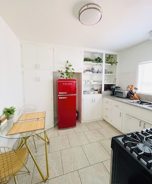 A compact kitchen with white cabinets, a red Galanz refrigerator, a gas stove, and a small dining table with chairs. - Downtown Studio: Free On-Site Parking • Beach & Convention Center One Mile (Long Beach)