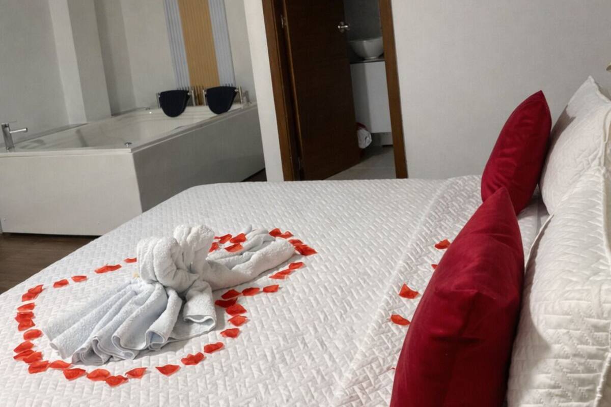 A hotel room with a bed, a red pillow, and a towel arrangement on the bed.
