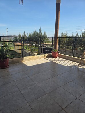 Un balcon doté d’un sol carrelé, de plantes en pot et d’une rambarde en métal.