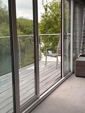 Ein Balkon mit Glastüren, einer gepolsterten Sitzecke und Blick auf Bäume.