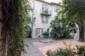 Une cour intérieure avec un bâtiment doté d’un balcon, de plantes en pot et d’un chemin pavé.