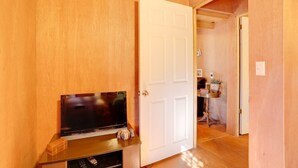 Une pièce avec un mur en bois, une porte blanche, un téléviseur à écran plat posé sur un meuble en bois, et une petite table sur laquelle se trouvent une plante et des livres.